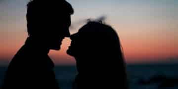 silhouette of man and woman about to kiss on beach during sunset