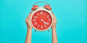 person holding red and beige twin bell analog alarm clock